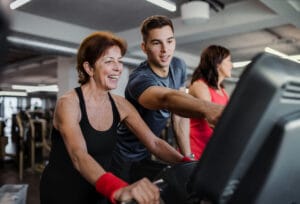 Senior woman working out in a gym and a personal trainer - personal training for seniors